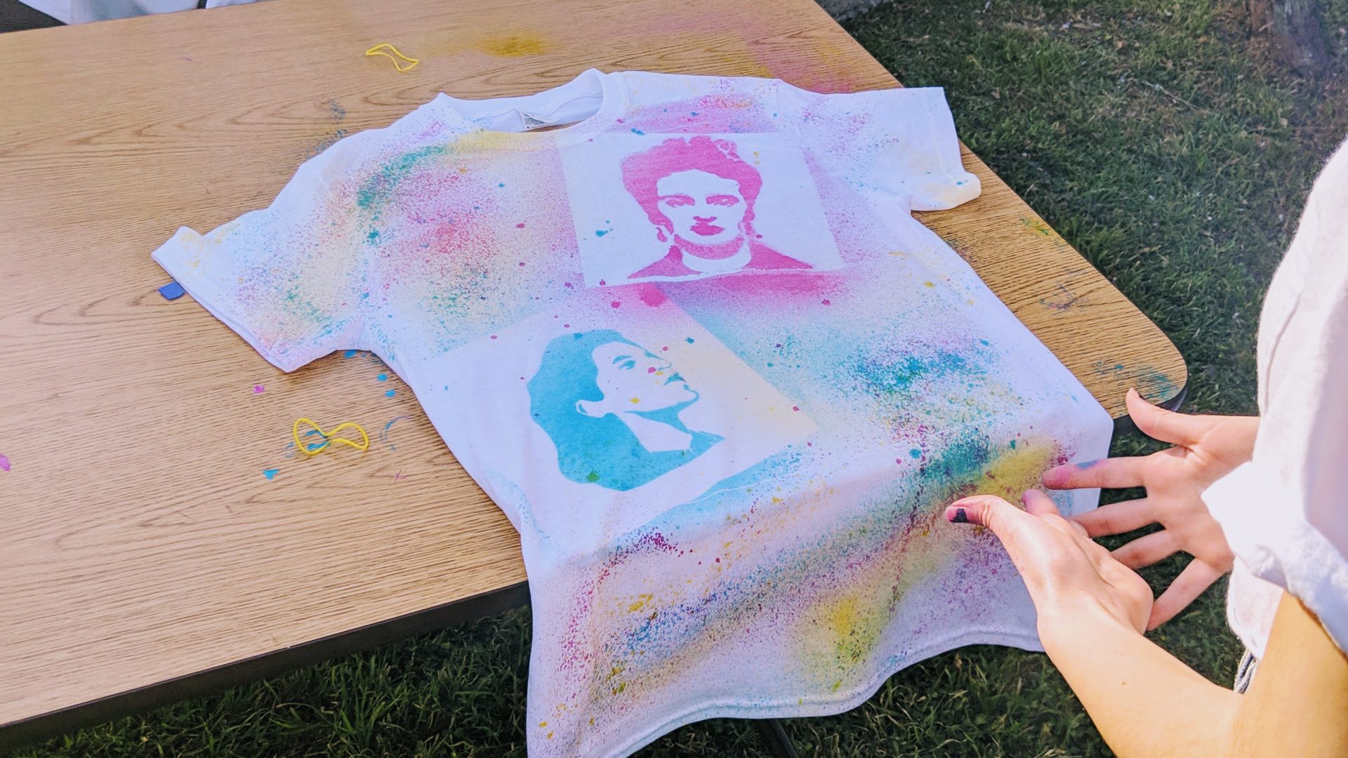 Hands holding a spraypainted stenciled shirt with Emma Tenayuca and Frida Kahlo